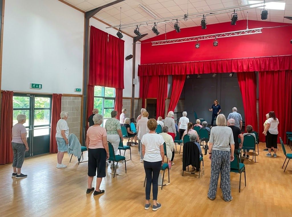Older adults taking part in a standing exercise class in a village hall